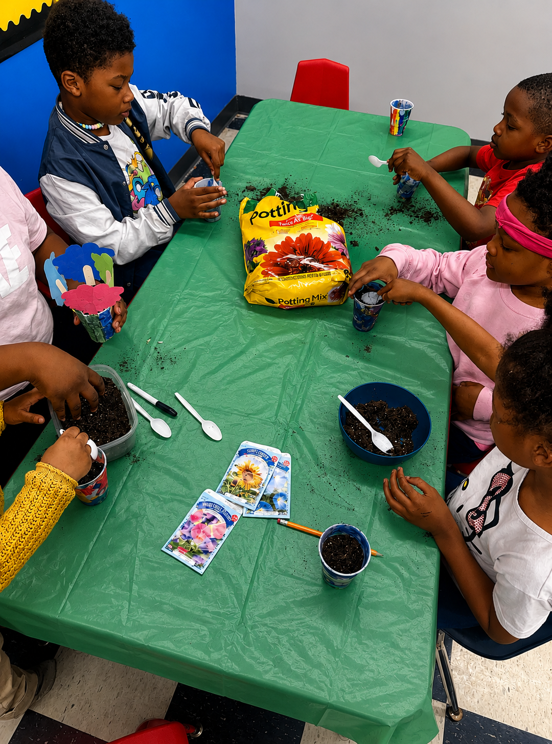 Children planting seeds in cups with potting soil at a classroom table