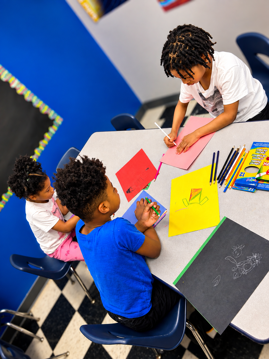 School-age children drawing and coloring on bright construction paper at a classroom table