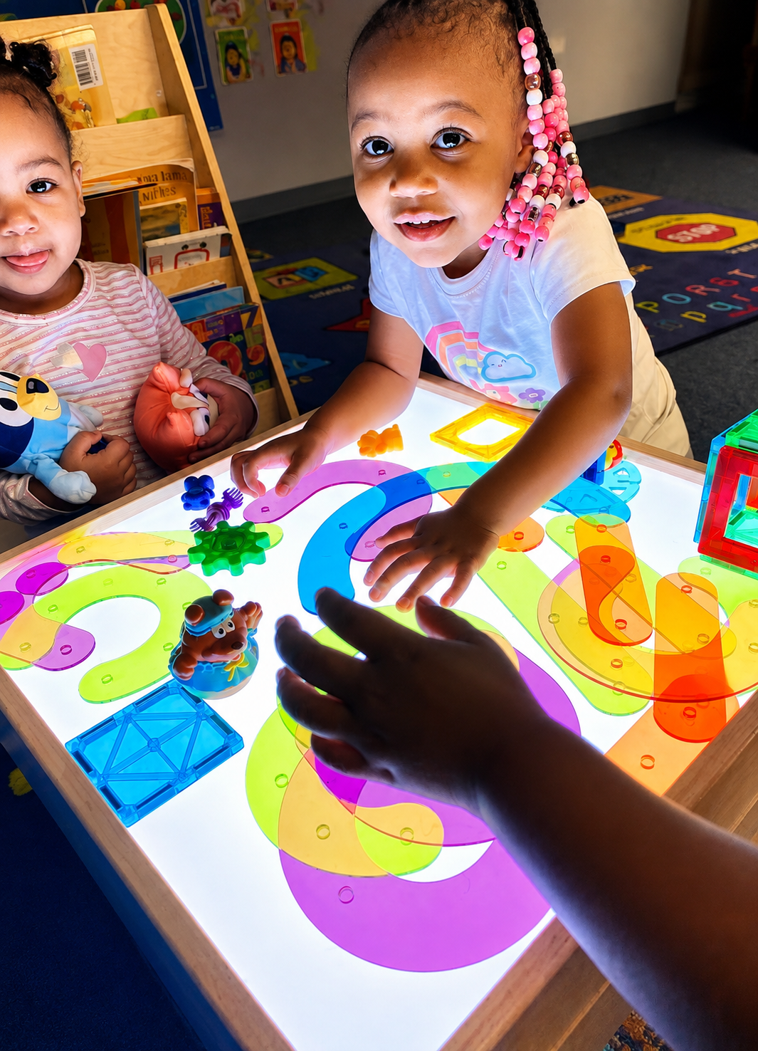 Toddlers playing with colorful translucent shapes on a glowing light table